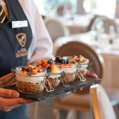 a breakfast service featuring individual yogurt and granola parfaits layered in small glass jars topped with fresh fruit and berries, being carried on a slate platter at The Rine in County Clare, Ireland