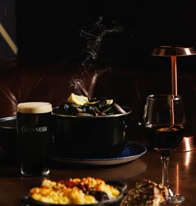 a classic Irish pub meal pairing a fresh pint of Guinness stout with a pot of steamed mussels, artisanal brown bread, macaroni bake, and a glass of red wine.